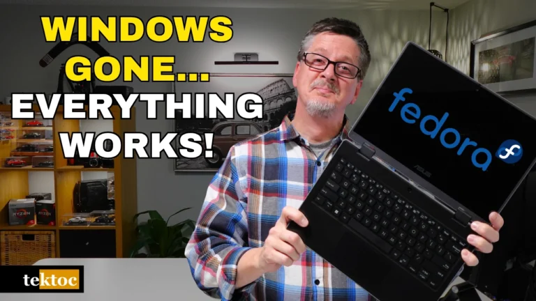 Graeme from tektoc holding an Asus BR1100 2-in-1 touch screen laptop running Fedora Linux, with the text "Windows Gone… Everything Works!"
