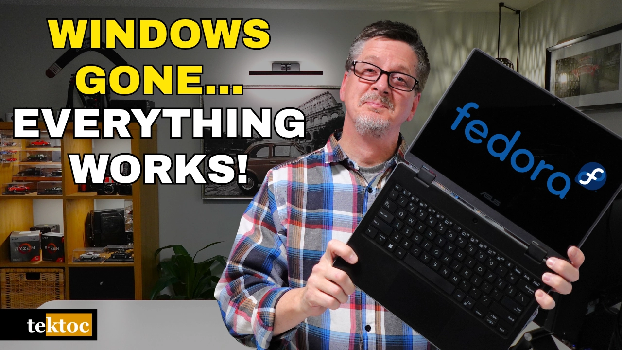 Graeme from tektoc holding an Asus BR1100 2-in-1 touch screen laptop running Fedora Linux, with the text "Windows Gone… Everything Works!"